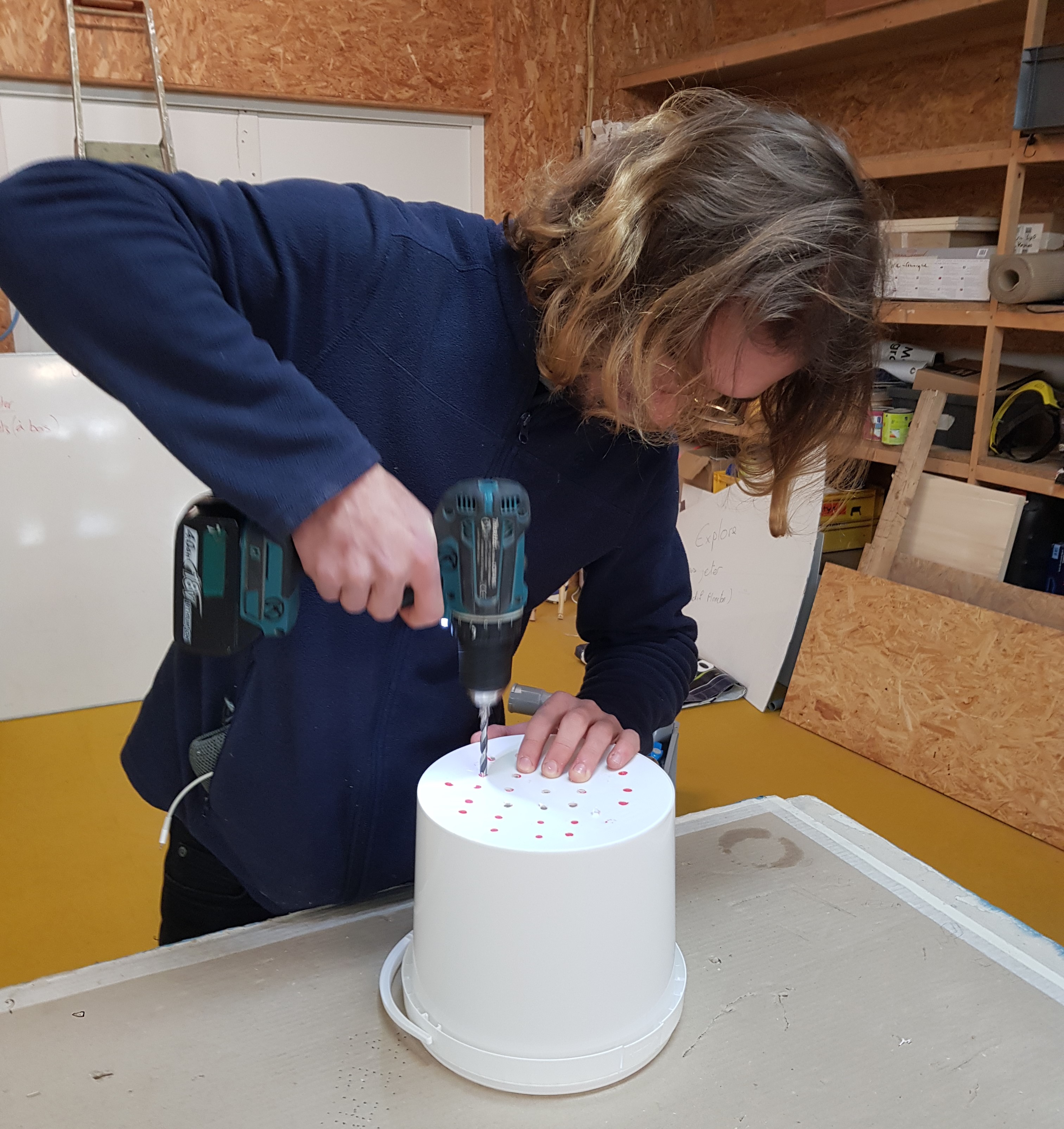 Maël en train de percer des trous dans un seau pour fabriquer un bokashi